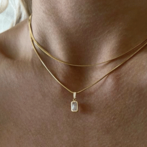 Tweelaagse goude ketting getoond op model. De onderste ketting heeft een bedel met een wit steentje.